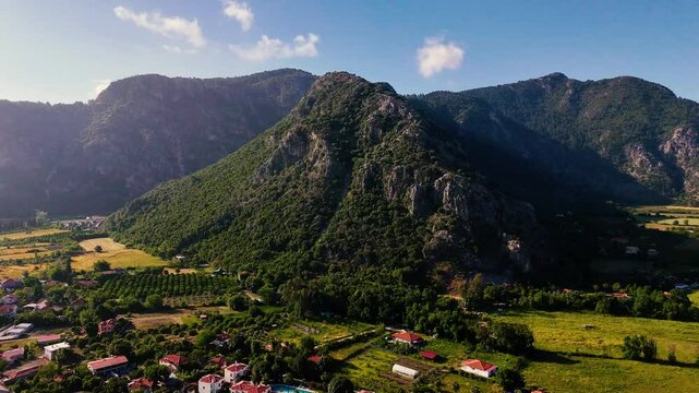Drone video capturing the serene landscape of Ortaca, with houses nestled amidst greenery and a majestic mountain backdrop