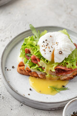 Toasted bread with poached egg, salad, cheese and ham on a plate on white kitchen background close up. Healthy breakfast, diet food
