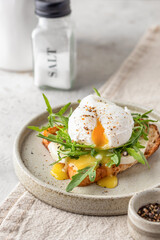 Toasted bread with poached egg, cheese and arugula on a plate on linen tablecloth background. Healthy breakfast, diet food