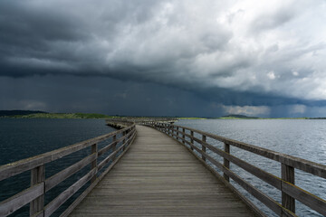 The photo shows a pier leading into calm waters, while dramatic storm clouds create a gloomy mood.