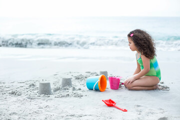 Female child kneeling molding sand towers at beach with colorful buckets and red spade, copy space