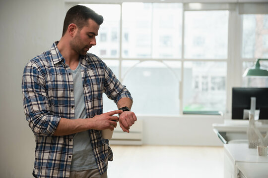 Man checking smartwatch in modern office by large windows with monitor and green lamp, copy space