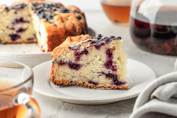 A piece of blueberry cake on a plate on light gray background, sweet breakfast or brunch, tea time