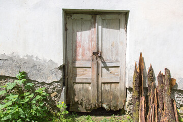 Old weathered wooden door with peeling paint and decaying bottom set in a cracked concrete wall...