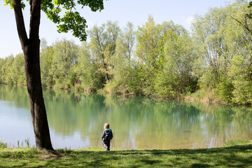 Little child by a calm lake in springtime forest, enjoying nature and peaceful solitude.