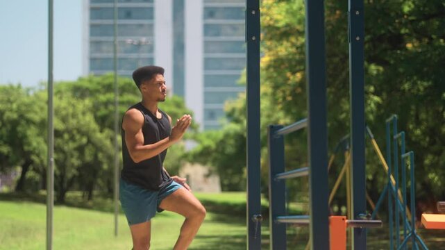 Focused African American man performing quick and intense high-knees exercise in an outdoor fitness park with urban buildings in the background
