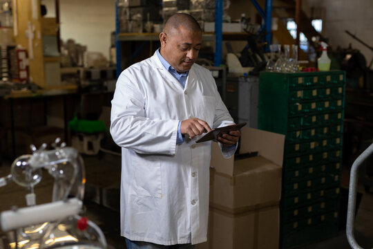 African American man inspecting apparatus using tablet in workshop with cardboard boxes green bins