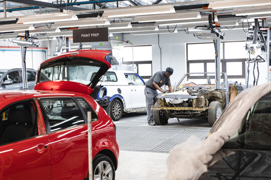 African American male auto body technician sanding chassis under paint prep sign near red hatchback