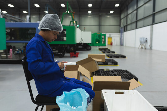 Asian man wearing hair net, coveralls packing components in cardboard boxes in factory, copy space