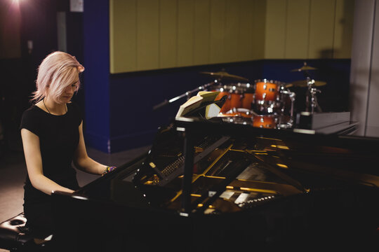 Female pianist playing grand piano in music studio near drum kit and sheet music, copy space