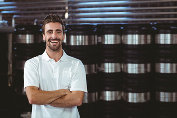 Man standing in brewery among steel kegs on racks wearing white polo shirt, copy space