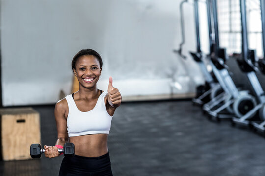 African American woman wearing sportswear holding dumbbell training at gym by rowers and plyo box