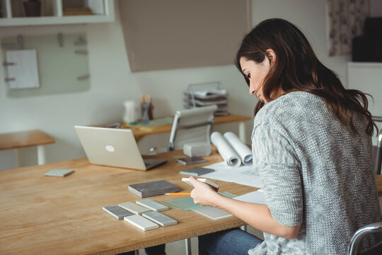 Material swatches lying on wooden desk and laptop displaying blueprints in design studio