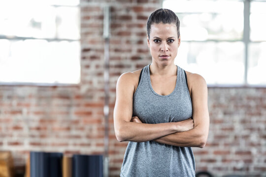 Mid adult woman standing in brick-walled gym wearing tank top beside rolled mats on bench