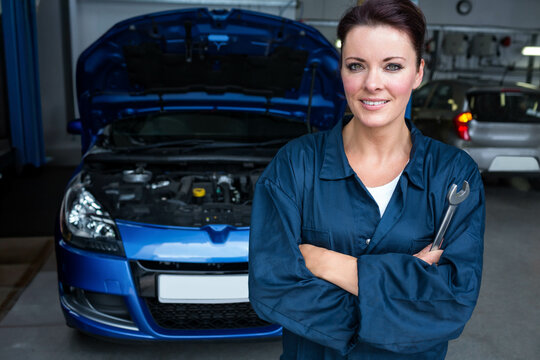 Female auto technician leaning on wrench by blue hatchback with open hood in garage, copy space