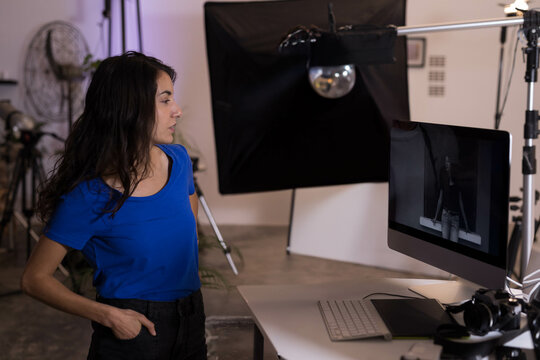 Woman reviewing monitor visuals in studio with keyboard and tablet, headphones, softbox, copy space