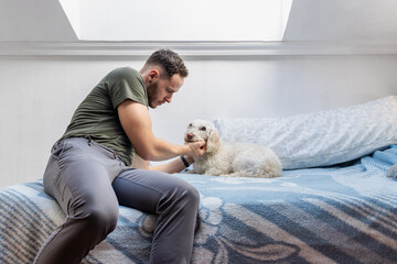 Man sitting on bed playing with his dog at home