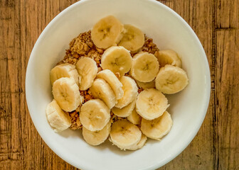Granola Cereal Topped With Sliced Bananas In A White Bowl