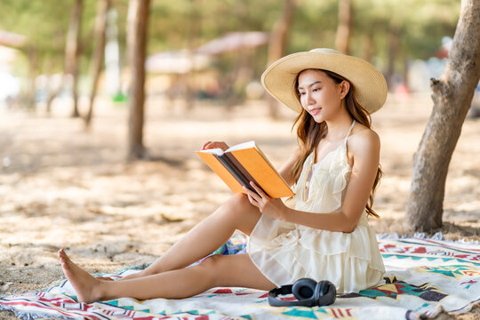 Happy Asian woman travel the sea on summer beach holiday vacation. Attractive girl enjoy outdoor lifestyle travel nature, social media detox relaxing and reading a book on tropical beach in sunny day.
