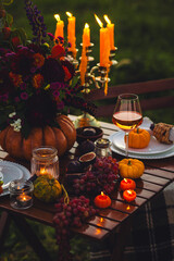 Fall table decoration with pumpkin composition. Family cozy thanksgiving dinner arrangement outdoors, in a garden, elegant wedding decor. Countryside style, rose wine, cheeseboard, fruits, autumn mood