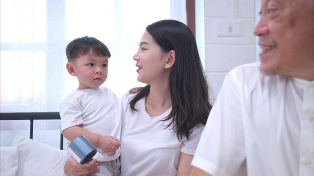 Before putting the kids to bed, mother, grandfather, and kid unwind and play in the bedroom