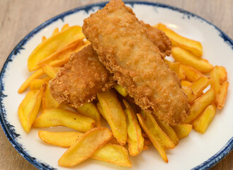 Fried fish fingers with french fries on a plate, close up