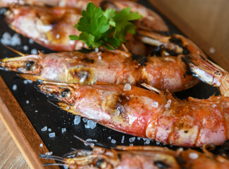 Grilled tiger prawns on a black plate with parsley