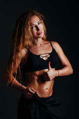 Young slim fitness woman showing thumbs up, portrait on black background