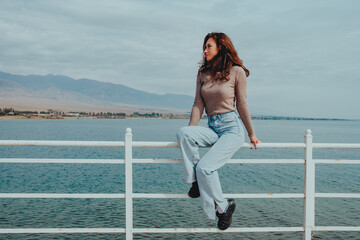 Young woman sitting on railing of bridge on lake shore