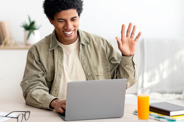 Online communication concept. Happy black teenager talking to his tutor or fellow students on laptop from home. African American guy waving and smiling during his video call on webcam