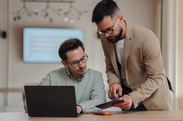 Two businessmen collaborating on project using laptop and tablet in office