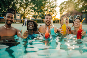 Friends toasting colorful drinks in swimming pool during summer party