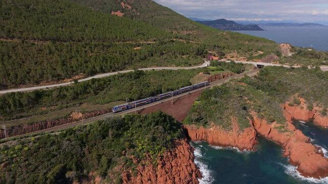 Aerial view of train crossing rugged terrain near Saint Raphael, France. Aerial drone video