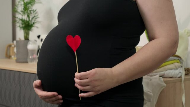 Pregnant woman holding red heart shape and feel love for unborn baby in belly. Awaiting for baby. Concept of maternity and pregnancy care