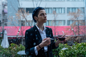 Young woman with wine glass standing outside in snowfall