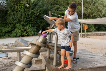 Happy brothers playing with Archimedes screw water system at outdoor playground on warm summer day. Concept of teamwork, child development, interactive science, and educational fun in public park.