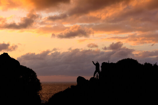 Man on rocks practicing tai chi chuan in front of the sea, silhouette of man walking with beautiful cloudy sky in the background.