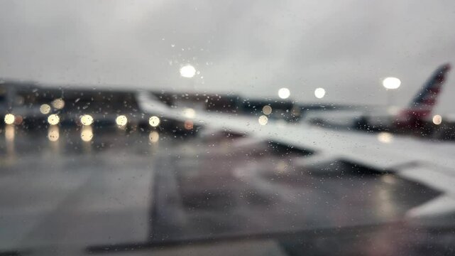  Rain drops on airplane window during rainy evening at New York airport with blurred aircraft lights. USA