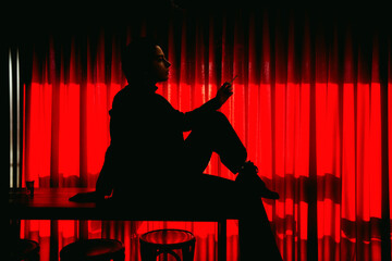 Art photography. Retro silhouette of girl in front of window. Noir photo. Woman smoking a cigarette in mouthpiece