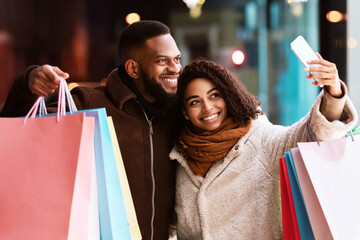 Entertainment And Fun Concept. Happy african american tow buyers taking selfie and showing shopping...