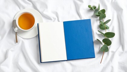 Blue Journal Beside Herbal Tea and Eucalyptus Leaves on White Fabric