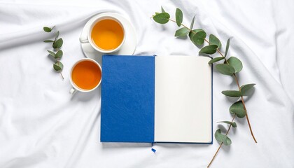 Blue Journal Beside Herbal Tea and Eucalyptus Leaves on White Fabric