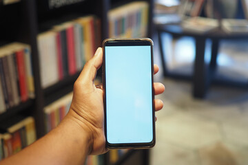 Hand holding smartphone in a cozy library environment