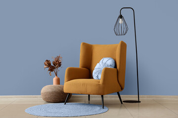 Armchair, lamp and pouf with flowers in vase near brown wall in room