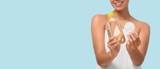 Beautiful young woman with bottle of micellar water and cotton pad on light blue background with...