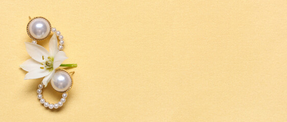 Stylish earrings and beautiful flower on yellow background