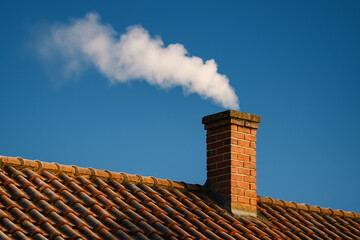 Brick chimney with smoke on tiled roof