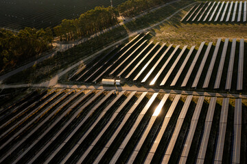 Obraz premium Drone view of extensive solar farm with rows of solar panels stretching across the landscape. Sunlight reflecting on dark surfaces of panels in late afternoon
