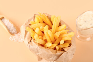 Paper bag with tasty french fries and salt on beige background