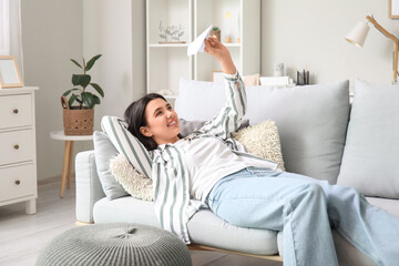 Young woman with paper plane lying on sofa at home